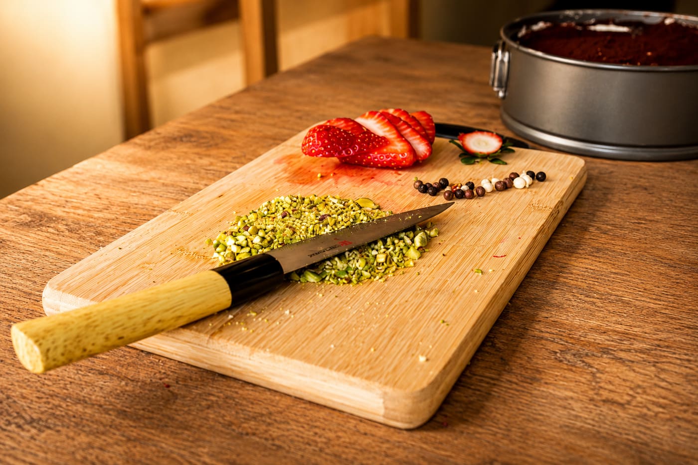 A chef's knife on a chopping board with crushed pistachios and strawberries in the Rai kitchen